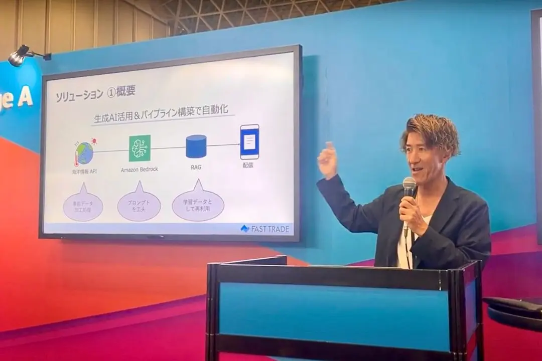 AWS Summit Japan 2024 のステージで、Amazon Bedrock を使った自動化パイプラインのスライドを背にマイクを持って登壇する福原玄