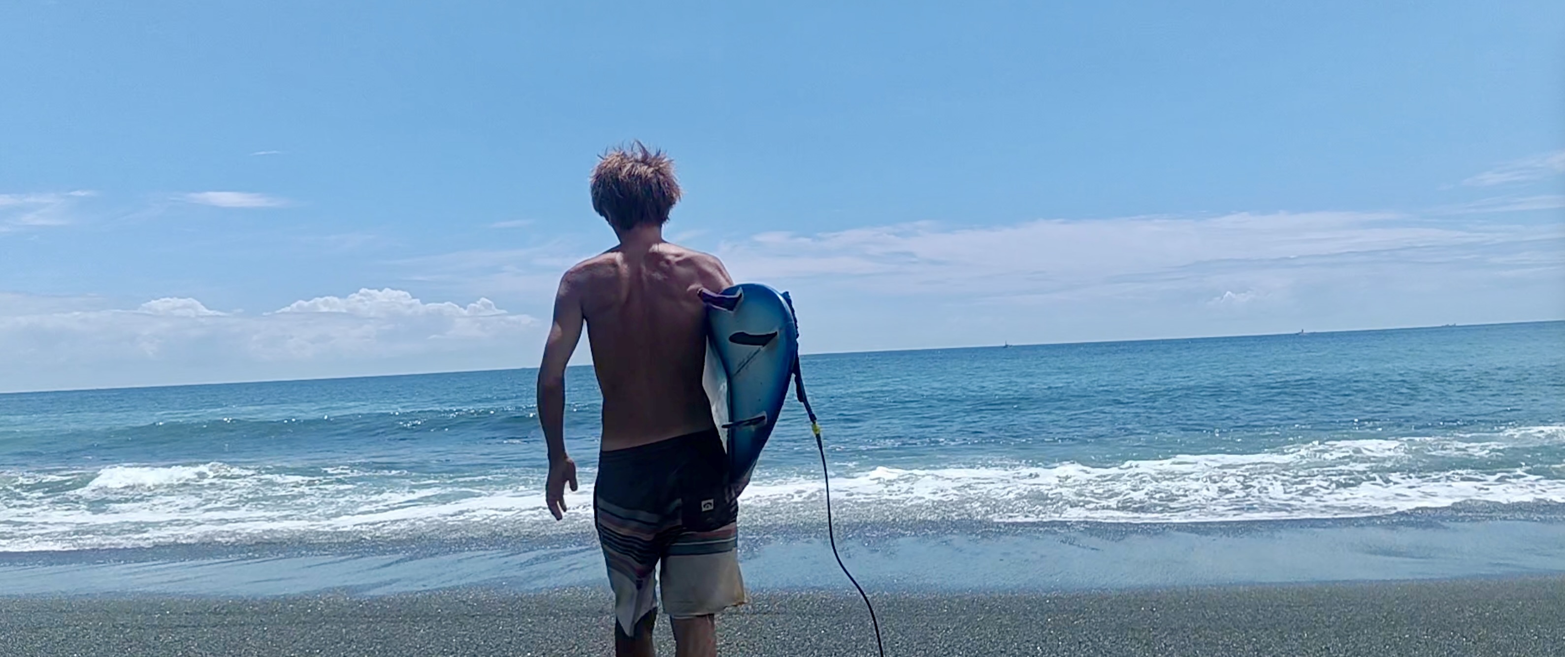 サーフボードを抱えて海に向かって歩く福原玄